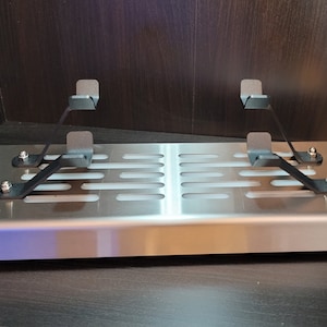 May include: A stainless steel shelf with a perforated design and two black metal brackets. The shelf is mounted to a wall and has a slight curve to the front edge.