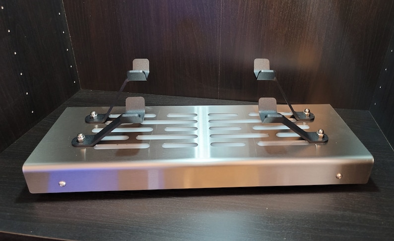 May include: A stainless steel shelf with a perforated design and two black metal brackets. The shelf is mounted to a wall and has a slight curve to the front edge.