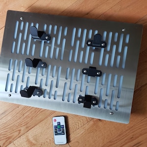 May include: A stainless steel wall-mounted rack with a grid pattern and five black metal hooks. A remote control is in the foreground.