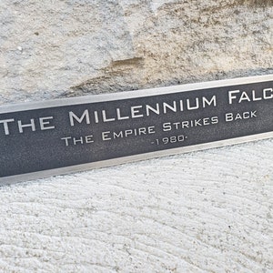 May include: A silver plaque with the text "THE MILLENNIUM FALCON THE EMPIRE STRIKES BACK -1980-."