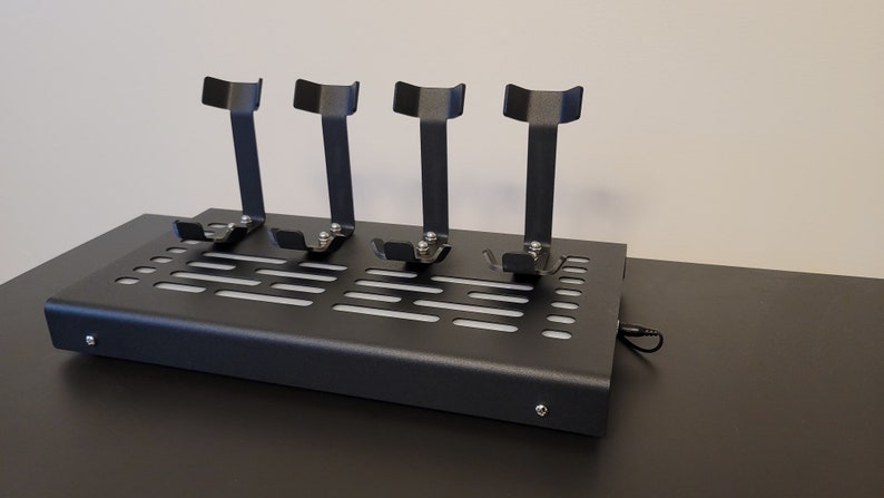 Pode incluir: Um suporte de metal preto com tr&ecirc;s suportes verticais para segurar fones de ouvido. O suporte tem uma base perfurada e um cabo preto.