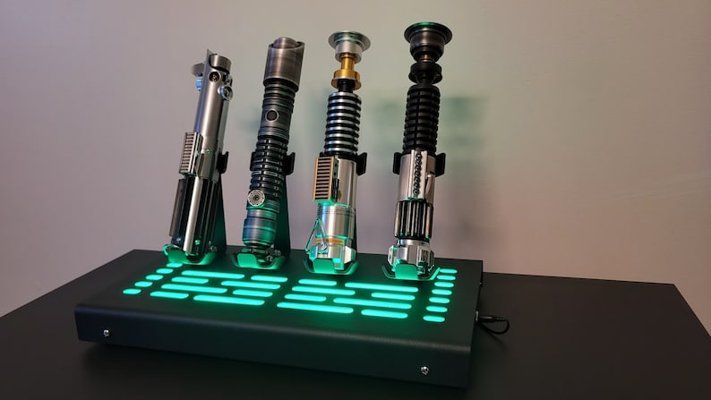 Pode incluir: Quatro r&eacute;plicas de sabres de luz em um suporte preto com uma luz verde. Os sabres de luz s&atilde;o prateados, pretos, dourados e verdes.