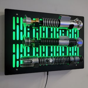 May include: A black wall mount with a green light-up Star Wars themed design. Three lightsabers are displayed on the mount.
