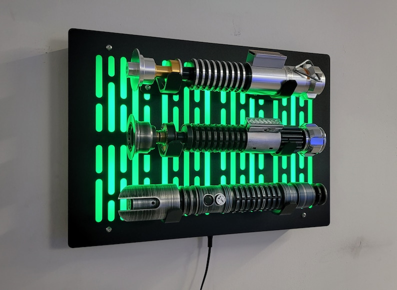 May include: A black wall mount with a green light-up Star Wars themed design. Three lightsabers are displayed on the mount.