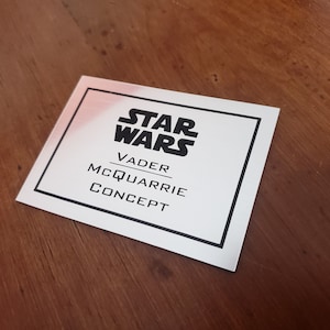 May include: A white card with black text that reads "Star Wars", "Vader", "McQuarrie", and "Concept".