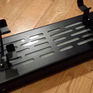 May include: Black metal stand with a grid pattern and two adjustable arms. The stand is designed to hold items upright.