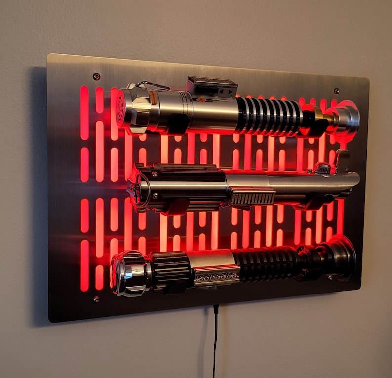 May include: A metal wall mount with a red light behind it, displaying three lightsabers. The lightsabers are silver and black with a red glow.