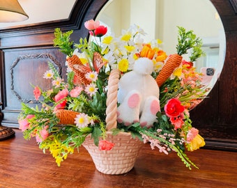 Peut inclure: Un panier en osier rose rempli d'une variété de fleurs de printemps, y compris des fleurs roses, blanches et jaunes. Un lapin blanc aux pieds roses est assis au centre du panier.
