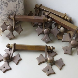 May include: Set of six antique brass drawer pulls with a cross design. Each pull has a square bar and a decorative cross-shaped end with a round knob in the centre.