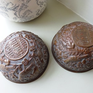 May include: Two antique copper bowls with intricate floral and bird designs. The bowls have a raised circular design in the center with Chinese characters.
