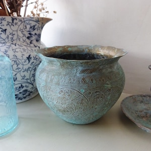 Może przedstawiać: Zwietrzała, turkusowa metalowa miska ze skomplikowanymi wytrawionymi wzorami. Miska ma zaokrąglony kształt z falistym brzegiem. Powierzchnia wykazuje oznaki wieku i utlenienia. Dekoracja domu.