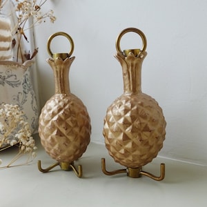 May include: Two gold pineapple-shaped bottle stoppers with a textured surface and a gold metal base.