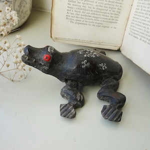 May include: A carved wooden frog figurine with red eyes and decorative white swirls. The dark brown frog has detailed legs and a textured body. The figurine is a unique decorative item.