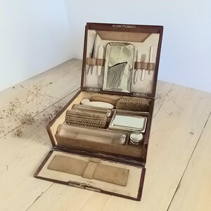 May include: Open brown leather travel grooming kit with a mirror, brushes, and various grooming tools. The kit is rectangular and has a hinged lid. The interior is lined with a light-colored fabric.