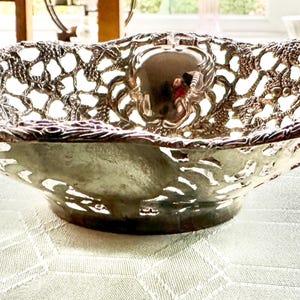 May include: An antique silver-coloured bowl with an intricate openwork design. The bowl features a scalloped edge and a round base. The detailed pattern is visible across the surface, creating a delicate and elegant appearance. This decorative bowl is suitable for serving or display.