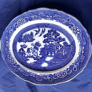 Puede incluir: Plato ovalado para servir con un diseño azul y blanco de patrón Willow. El plato presenta una escena central de paisaje con un puente, árboles y edificios, rodeada por un borde decorativo. El plato mide aproximadamente 40 cm de largo.