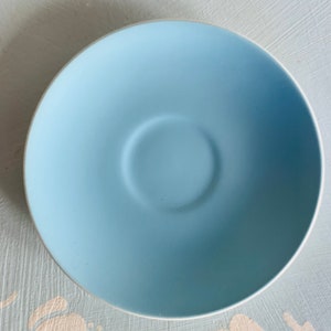 May include: A pale blue saucer with a white edge. The saucer features a central indentation for a teacup. The colour is a soft, pastel blue, and the rim is white. This saucer is likely part of a tea set, suitable for serving tea.
