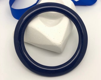 May include: A dark blue bangle bracelet made of smooth, glossy plastic.