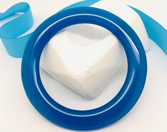 May include: A bright blue bangle bracelet made of resin. The bracelet is thick and has a smooth, glossy finish.