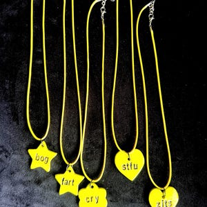 Può includere: Sei collane gialle con catene argentate. Ogni collana presenta un ciondolo giallo con una parola o frase in un colore a contrasto. I ciondoli hanno forme di stella, fiore e cuore, con parole come "bog", "fart", "cry", "stfu" e "zits".