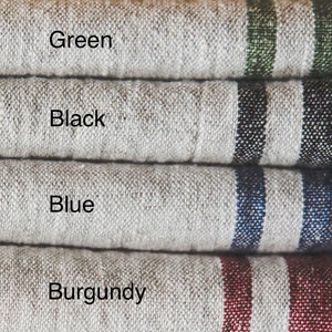May include: Four stacked pieces of textured beige fabric, each featuring two vertical stripes in different colors. The text labels identify the colors as Green, Black, Blue, and Burgundy, corresponding to the stripe color on each fabric layer.