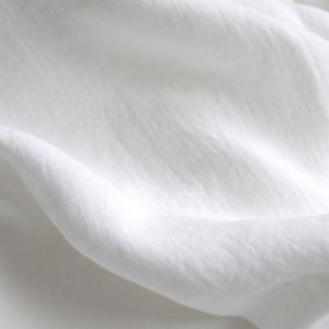 May include: White linen fabric with a smooth, soft texture. The fabric is folded and draped, creating a gentle wave pattern.