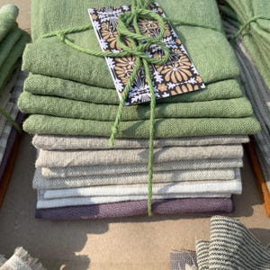 May include: A stack of green, beige, and purple fabric squares tied together with twine. A small card with a floral pattern is tied to the twine.