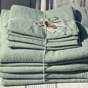 May include: A stack of sage green linen fabric sheets tied together with twine and decorated with wooden buttons.