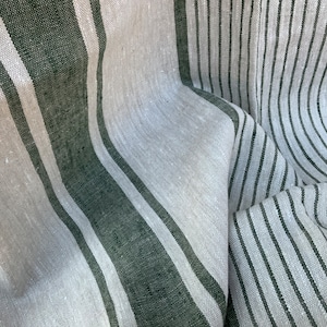 May include: Close-up of a linen fabric with a striped pattern. The fabric features alternating vertical stripes of light gray and dark green. The fabric is slightly wrinkled, suggesting a natural texture.