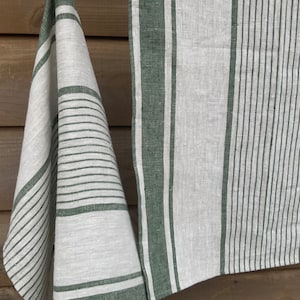May include: Two white linen tea towels with green stripes. The towels are hanging on a wooden wall.