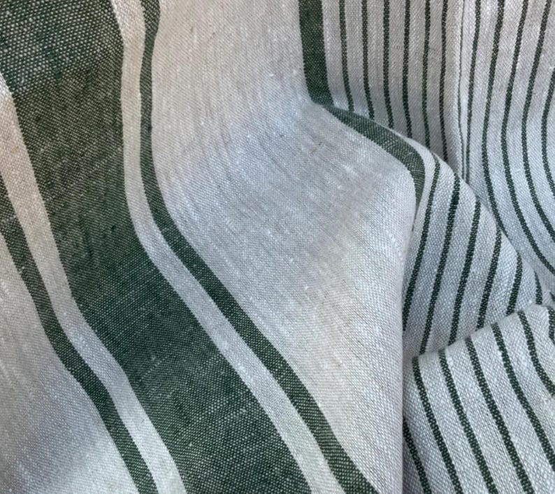 May include: A woven fabric featuring a pattern of alternating wide dark forest green stripes and narrower off-white stripes. The textile has a visible, slightly coarse, natural fibre texture with vertical lines running throughout the material.
