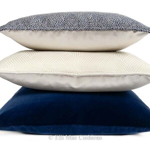 May include: Three decorative throw pillows stacked on top of each other. The top pillow is navy blue with white polka dots. The middle pillow is cream with a chevron pattern. The bottom pillow is a solid navy blue.