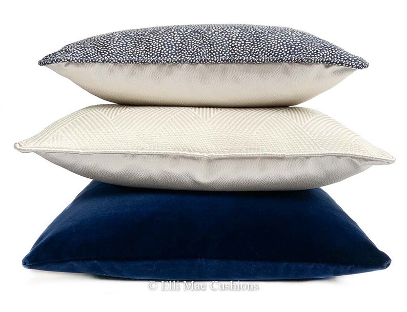 May include: Three decorative throw pillows stacked on top of each other. The top pillow is navy blue with white polka dots. The middle pillow is cream with a chevron pattern. The bottom pillow is a solid navy blue.