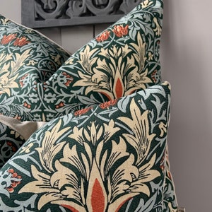 May include: Two green and cream patterned throw pillows with a floral design. The pillows are made of a soft, textured fabric and feature a repeating pattern of stylised flowers and leaves.