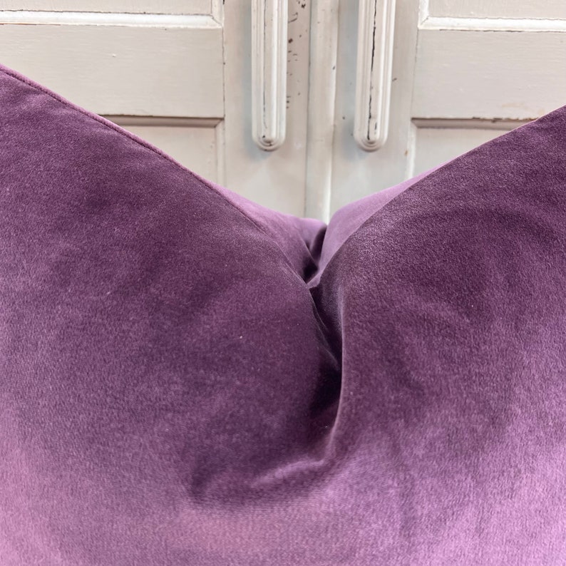 May include: A close-up of a purple velvet cushion. The cushion is soft and plush, with a subtle sheen.