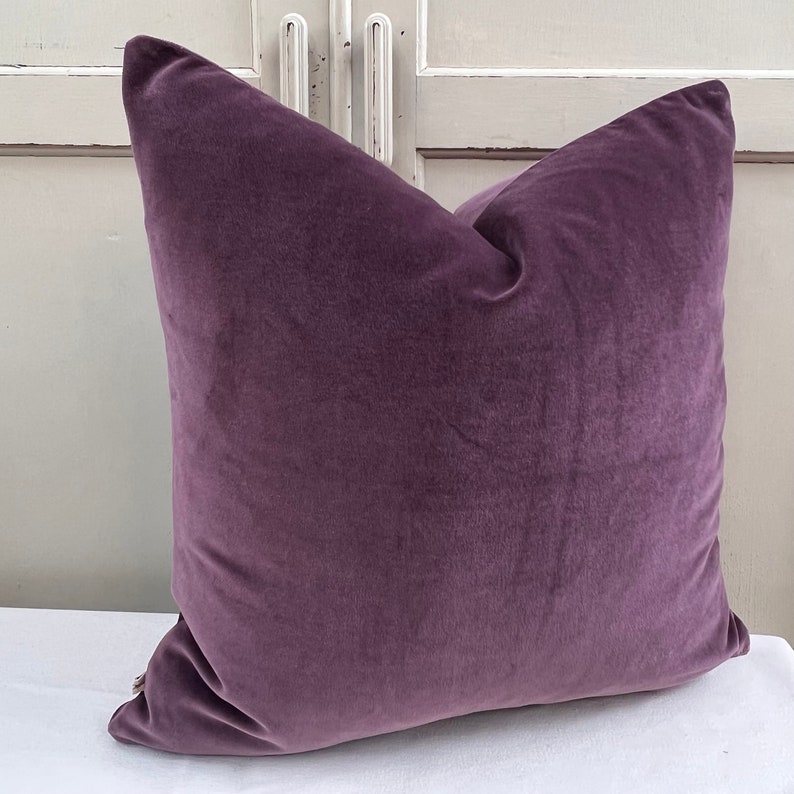 May include: A plush purple velvet cushion with a square shape. The cushion is soft and comfortable, perfect for adding a touch of luxury to any room.