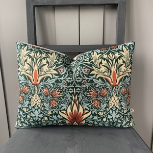 May include: A green, blue and orange patterned cushion with a floral design. The cushion is made of a soft, textured fabric.