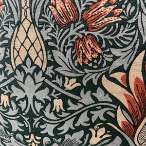 May include: A close-up of a fabric with a repeating pattern of stylised flowers and leaves in shades of green, brown, and cream. The fabric has a textured surface.