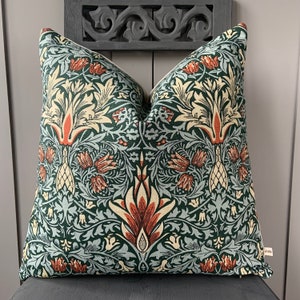 May include: A green, blue and orange patterned cushion with a floral design. The cushion is made of a soft, woven fabric.