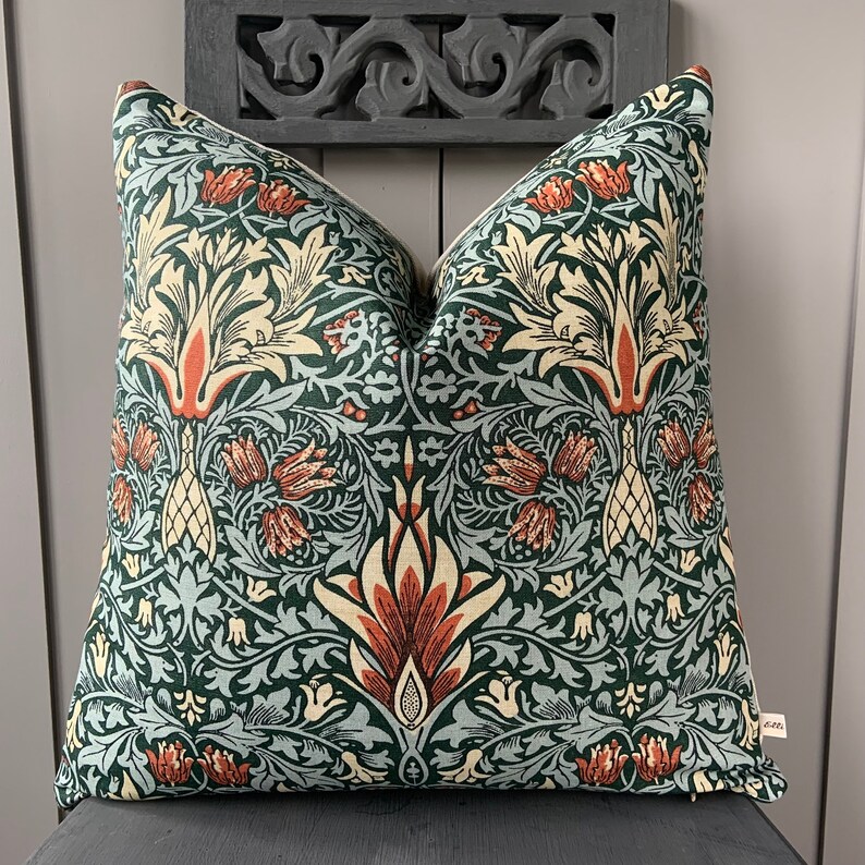 May include: A green, blue and orange patterned cushion with a floral design. The cushion is made of a soft, woven fabric.