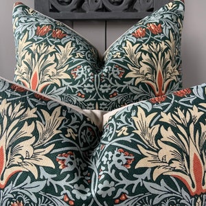 May include: Two green, cream and orange patterned throw pillows with a floral design. The pillows are arranged on a dark grey surface.
