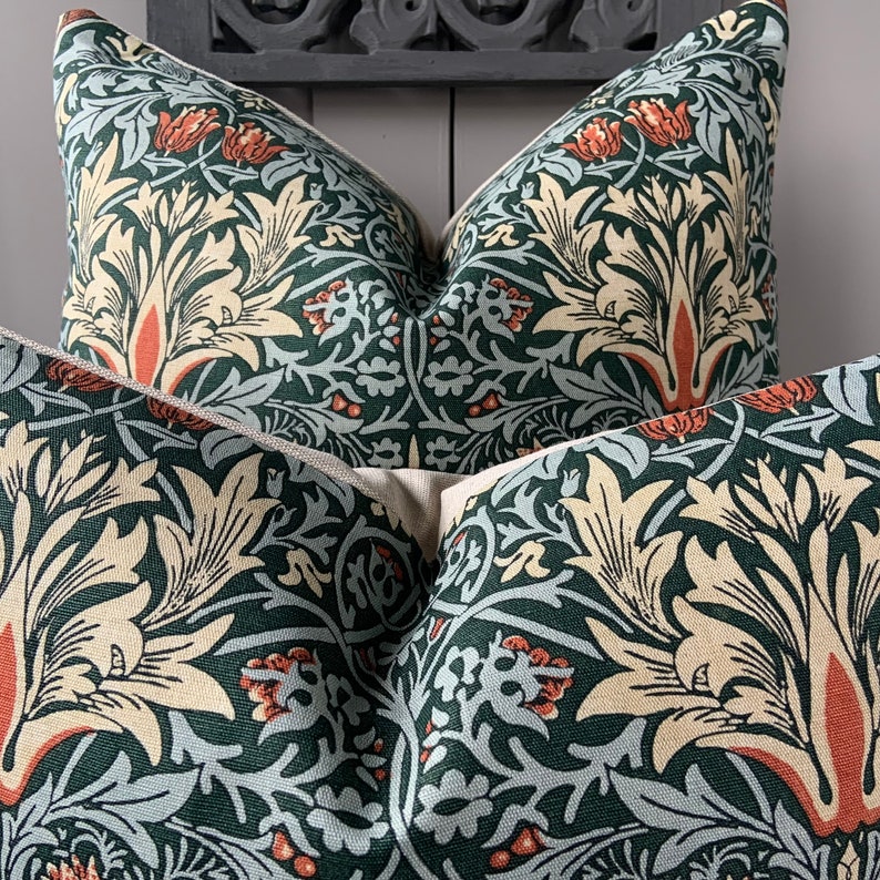 May include: Two green, cream and orange patterned throw pillows with a floral design. The pillows are arranged on a dark grey surface.