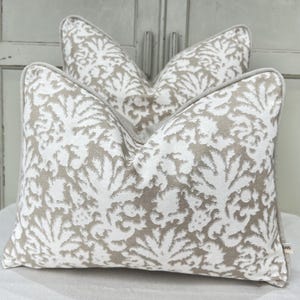 May include: Two decorative throw pillows with a beige and white floral pattern. The pillows have a light gray border and are arranged in a layered display. The fabric has a textured appearance, adding depth to the design.