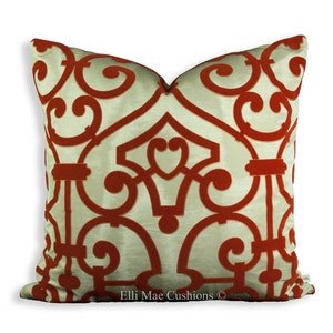Op de afbeelding: Een decoratief kussen met een crèmekleurige achtergrond en een rood geometrisch patroon. Het kussen heeft een herhalend ontwerp van gestileerde swirls en bogen. De tekst "Elli Mae Cushions ©" is afgedrukt op de onderkant van het kussen.