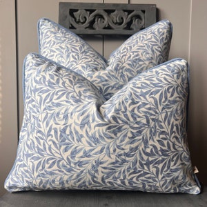 May include: Two blue and white patterned cushion covers with a light blue trim. The cushions are sitting on a dark grey surface.