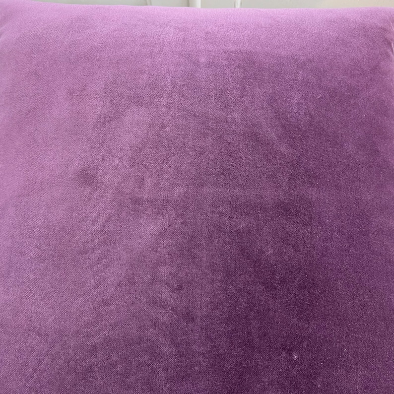 May include: A close-up of a soft, plush purple cushion. The fabric has a subtle texture and a slightly faded appearance.