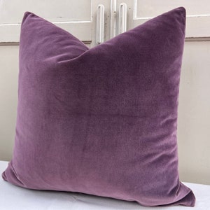May include: A plush purple cushion with a soft, velvety texture. The cushion is square-shaped and has a simple, elegant design.