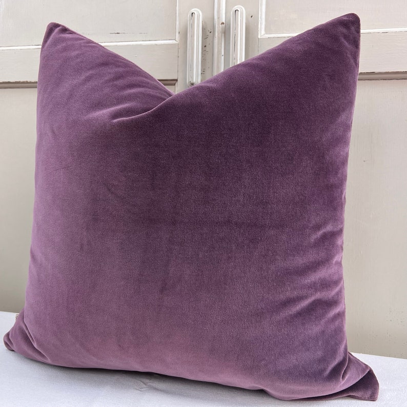 May include: A plush purple cushion with a soft, velvety texture. The cushion is square-shaped and has a simple, elegant design.