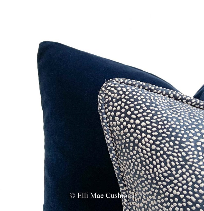 May include: Close-up of a navy blue velvet cushion with a white polka dot patterned cushion on top. The polka dot cushion has a navy blue border.