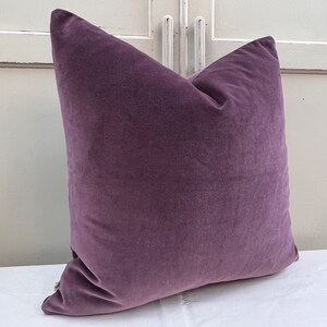 May include: A plush purple cushion with a soft, velvety texture. The cushion is square-shaped and has a subtle sheen.